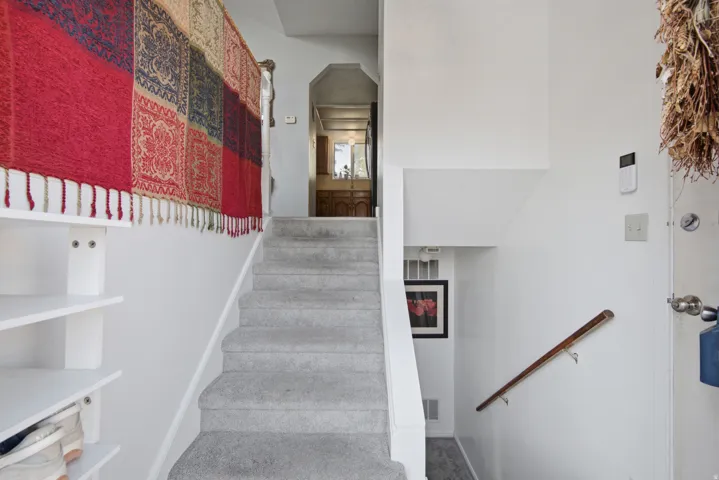 Carpeted staircase with a wood handrail leading to an upper level