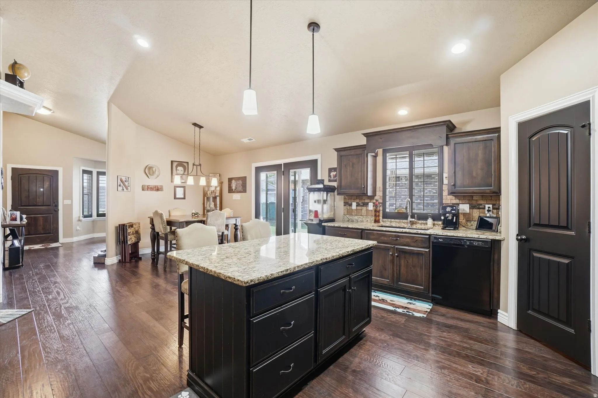 Kitchen featuring a breakfast bar, light stone counters, a kitchen island, dishwasher, and vaulted ceiling