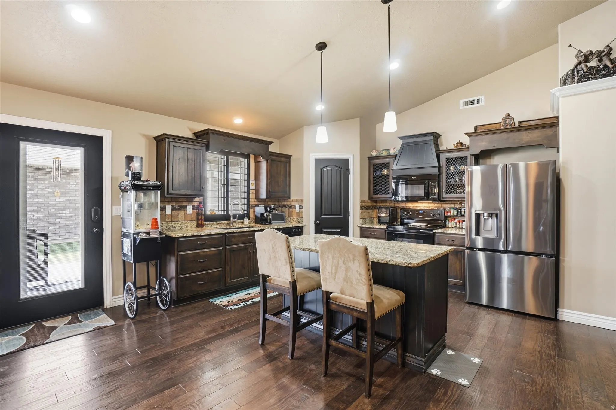 Kitchen with stainless steel fridge, decorative backsplash, light stone counters, black electric range, and dark wood finish cabinets