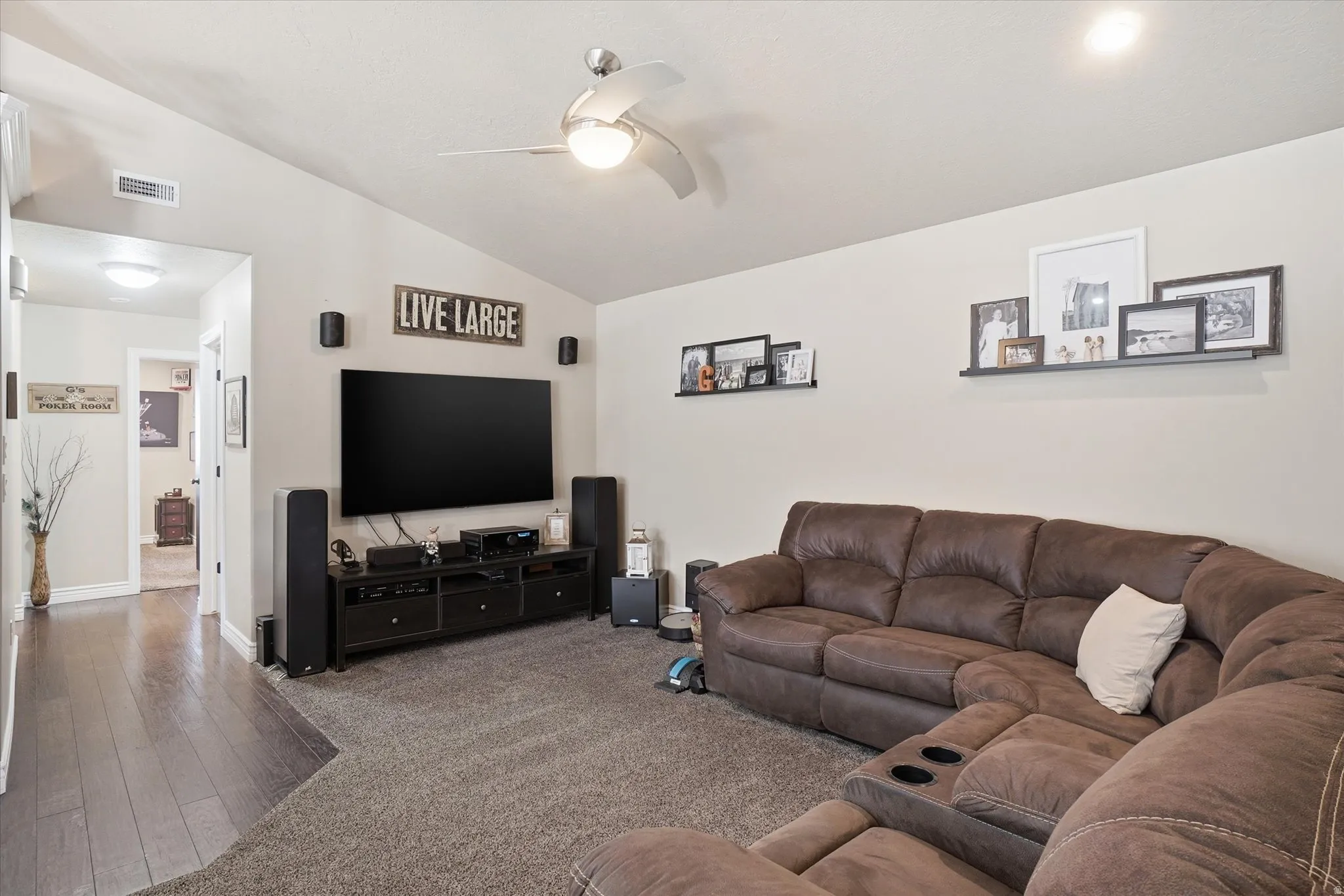 Carpeted living room with lofted ceiling, ceiling fan, and wood finished floors