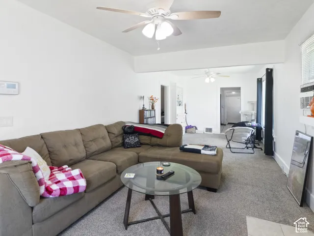 Spacious living area featuring light gray carpeting, crisp white walls, and a ceiling fan with integrated lighting