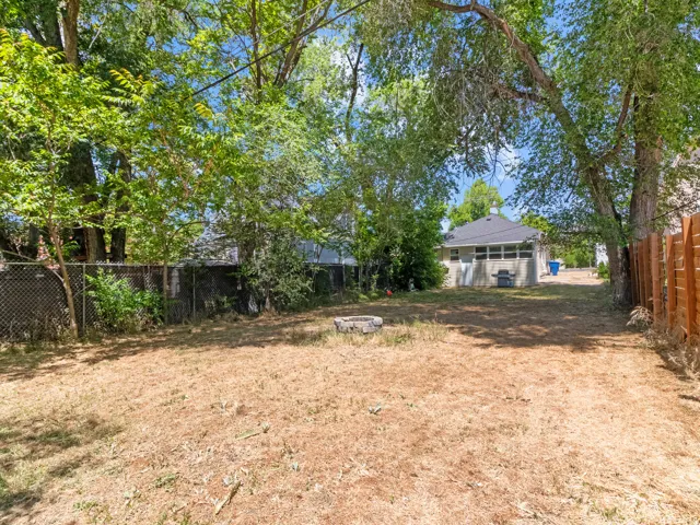 Spacious backyard featuring a stone fire pit, mature trees, and a combination of chain link and wood fencing