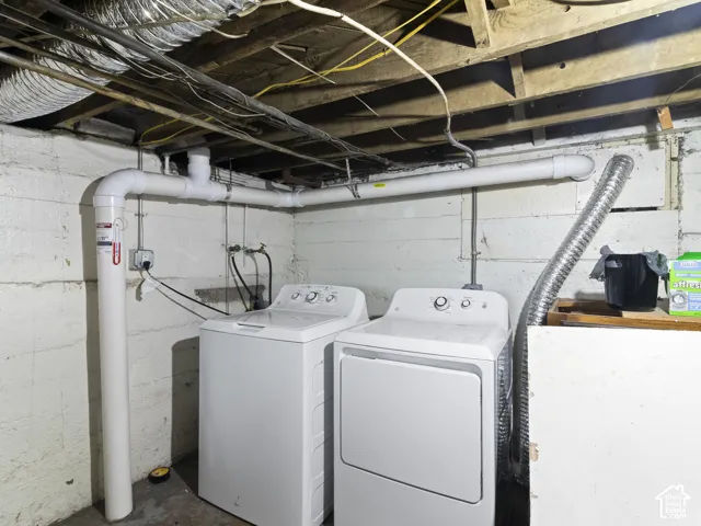 Dedicated laundry area featuring a white washing machine, white dryer, exposed ceiling joists, and concrete walls