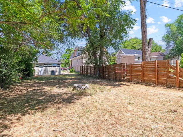 Expansive backyard with a modern horizontal slat fence, mature trees providing shade, and a stone-lined fire pit