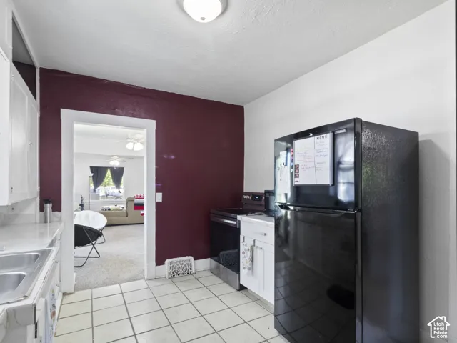 Kitchen featuring tile flooring, white cabinetry, a double basin sink, and a black refrigerator