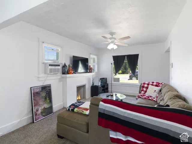 Living area featuring a fireplace with a white mantel, ceiling fan with light fixture, two windows, and carpeting