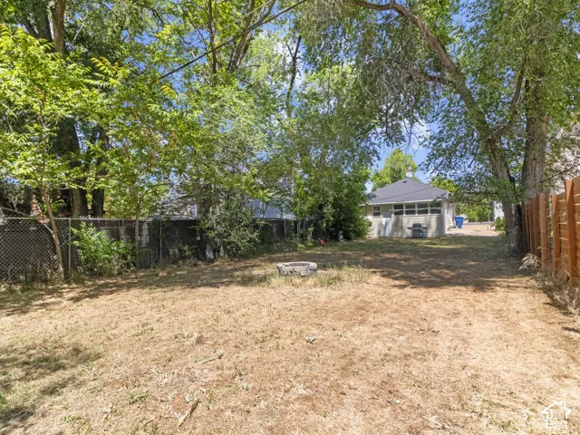 Spacious backyard featuring a stone fire pit, mature trees, and a combination of chain link and wood fencing