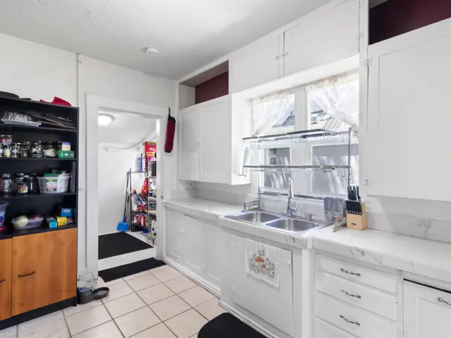 Kitchen featuring white upper and lower cabinetry, a double basin stainless steel sink, and light-toned countertops