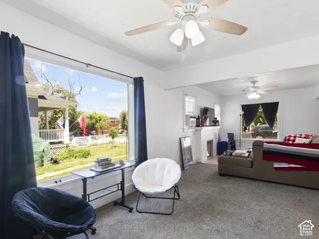 Spacious interior featuring a large picture window, ceiling fans, a white painted fireplace mantel, and gray carpet flooring