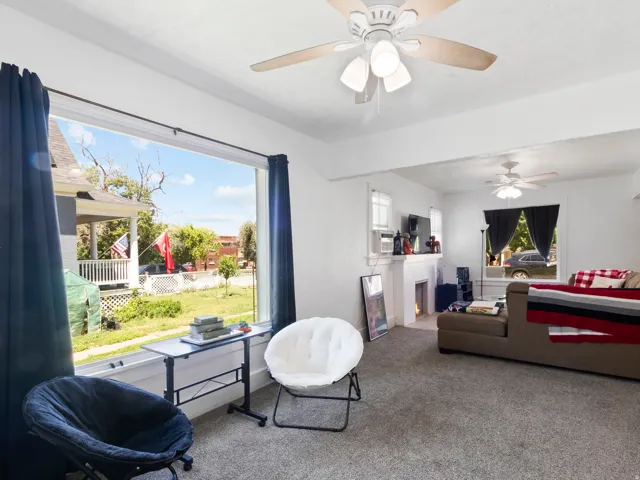 Spacious interior featuring a large picture window, ceiling fans, a white painted fireplace mantel, and gray carpet flooring