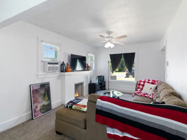 Living area featuring a fireplace with a white mantel, ceiling fan with light fixture, two windows, and carpeting
