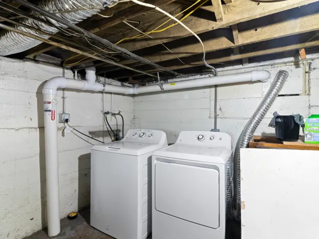 Dedicated laundry area featuring a white washing machine, white dryer, exposed ceiling joists, and concrete walls