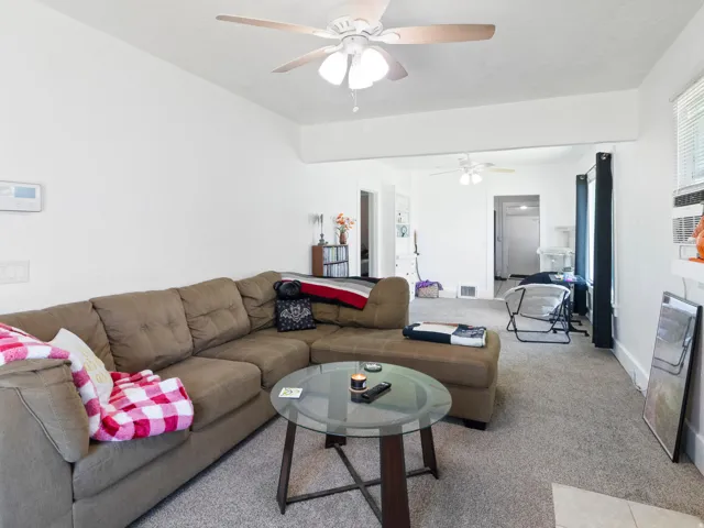 Spacious living area featuring light gray carpeting, crisp white walls, and a ceiling fan with integrated lighting