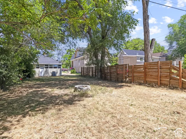 Expansive backyard with a modern horizontal slat fence, mature trees providing shade, and a stone-lined fire pit