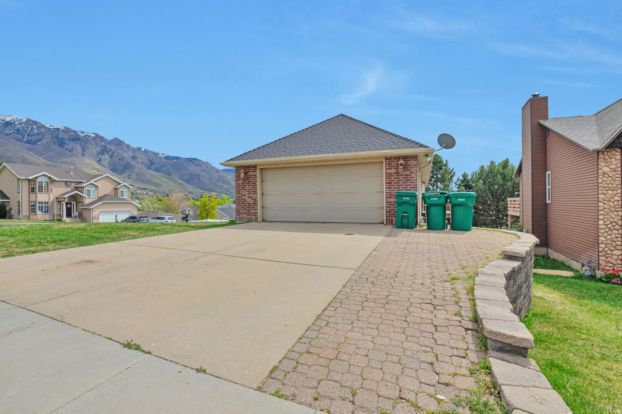 View of property exterior with brick siding, driveway, a garage, a mountain view, and a yard