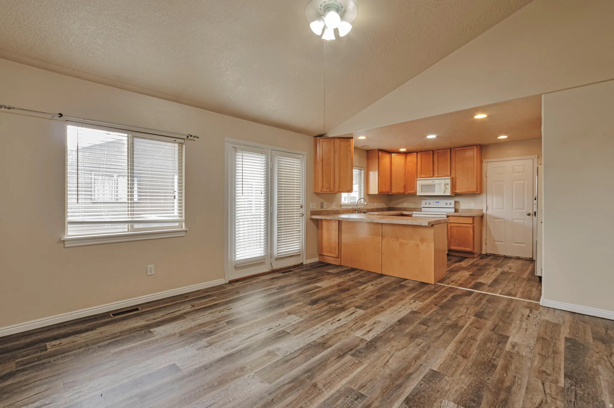 Kitchen featuring a peninsula, vaulted ceiling, light countertops, dark wood-type flooring, and white appliances