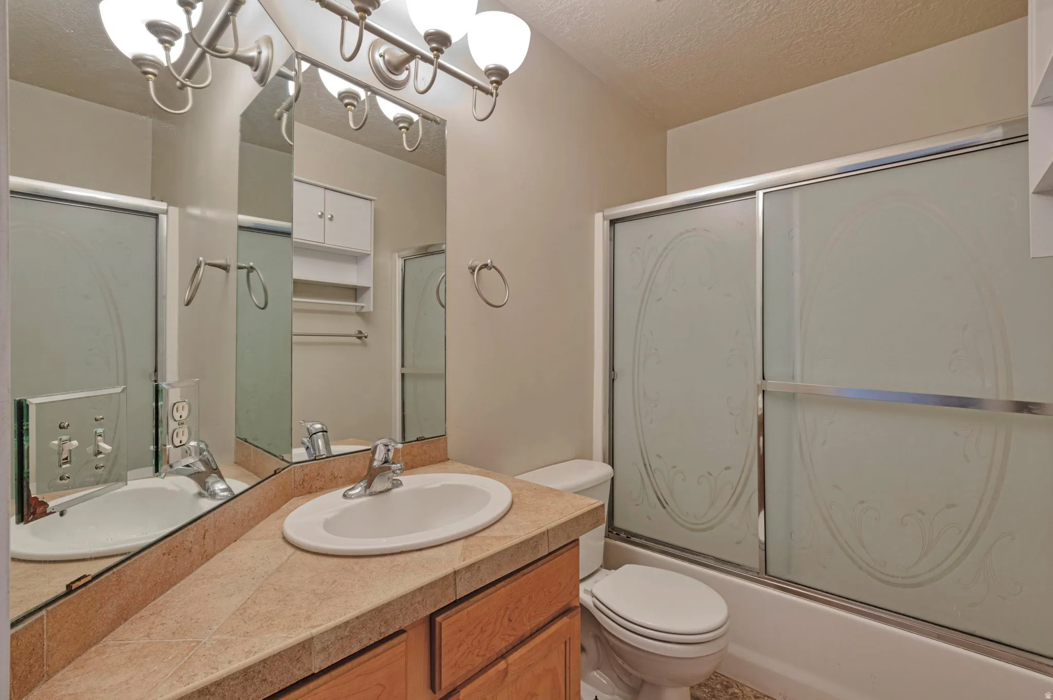 Bathroom featuring vanity, a textured ceiling, combined bath / shower with glass door, and hanging lights