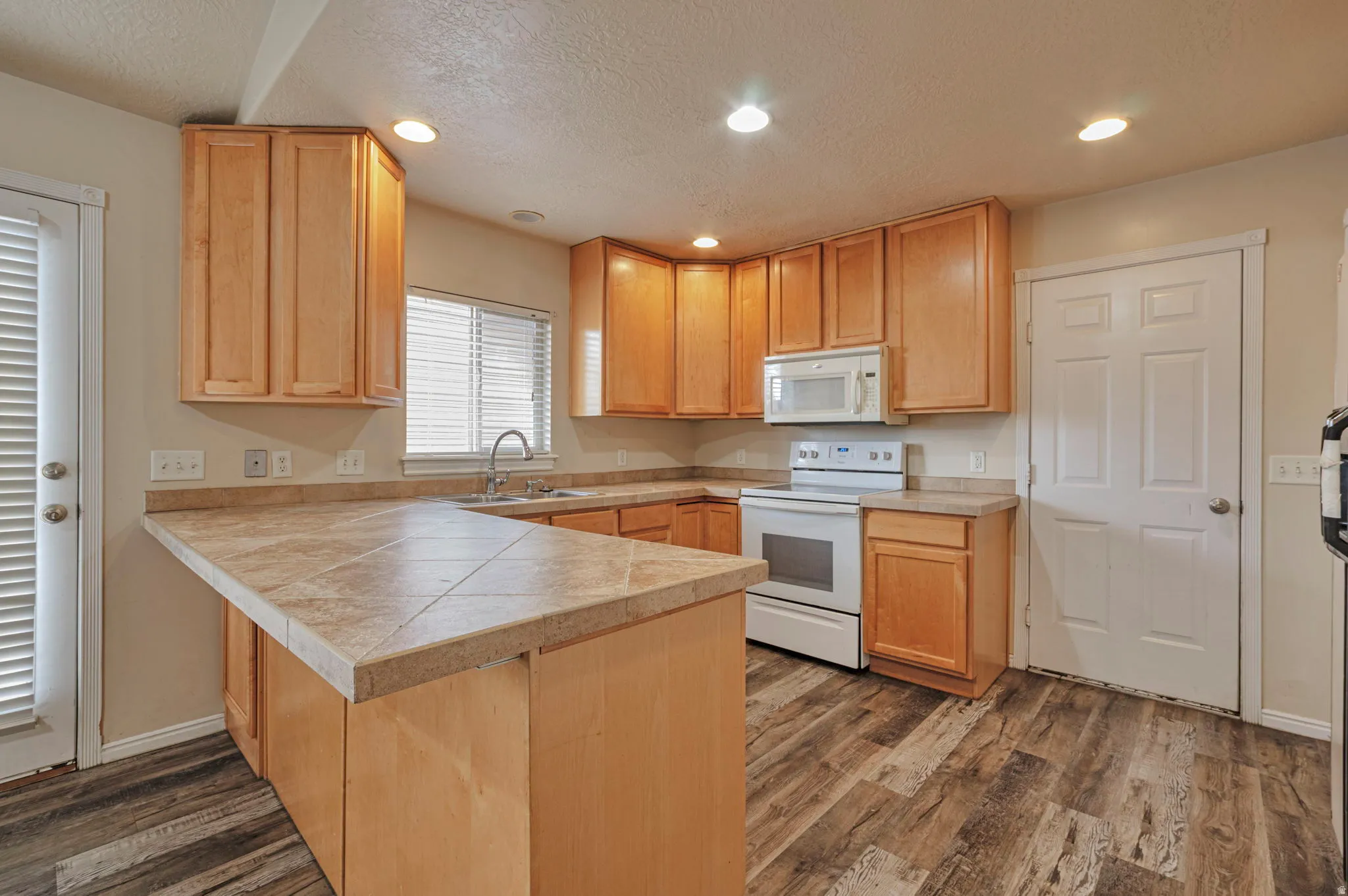 Kitchen featuring a peninsula, white appliances, recessed lighting, a textured ceiling, and dark wood finished floors