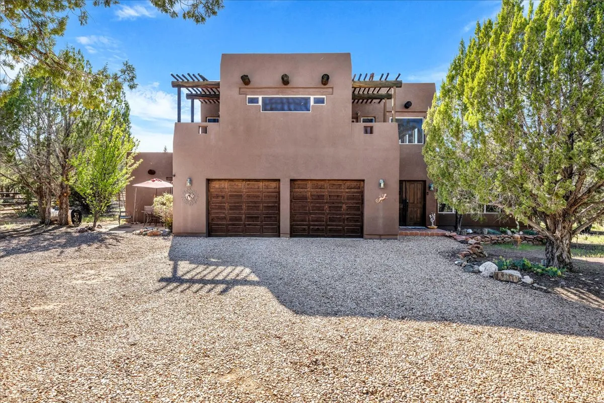 Pueblo-style house featuring an attached garage, stucco siding, and gravel driveway
