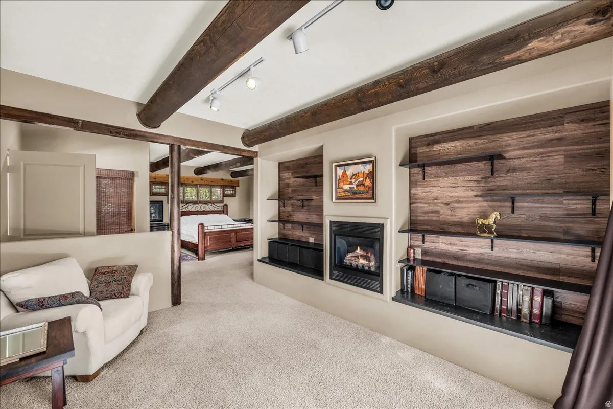Carpeted living area with track lighting, a glass covered fireplace, and beam ceiling