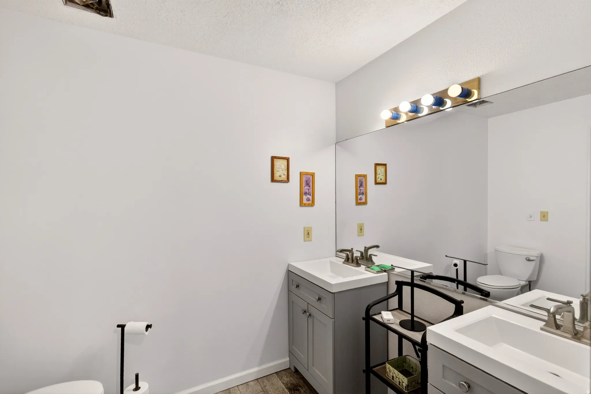 Bathroom featuring two vanities, light wood-type flooring, and a textured ceiling