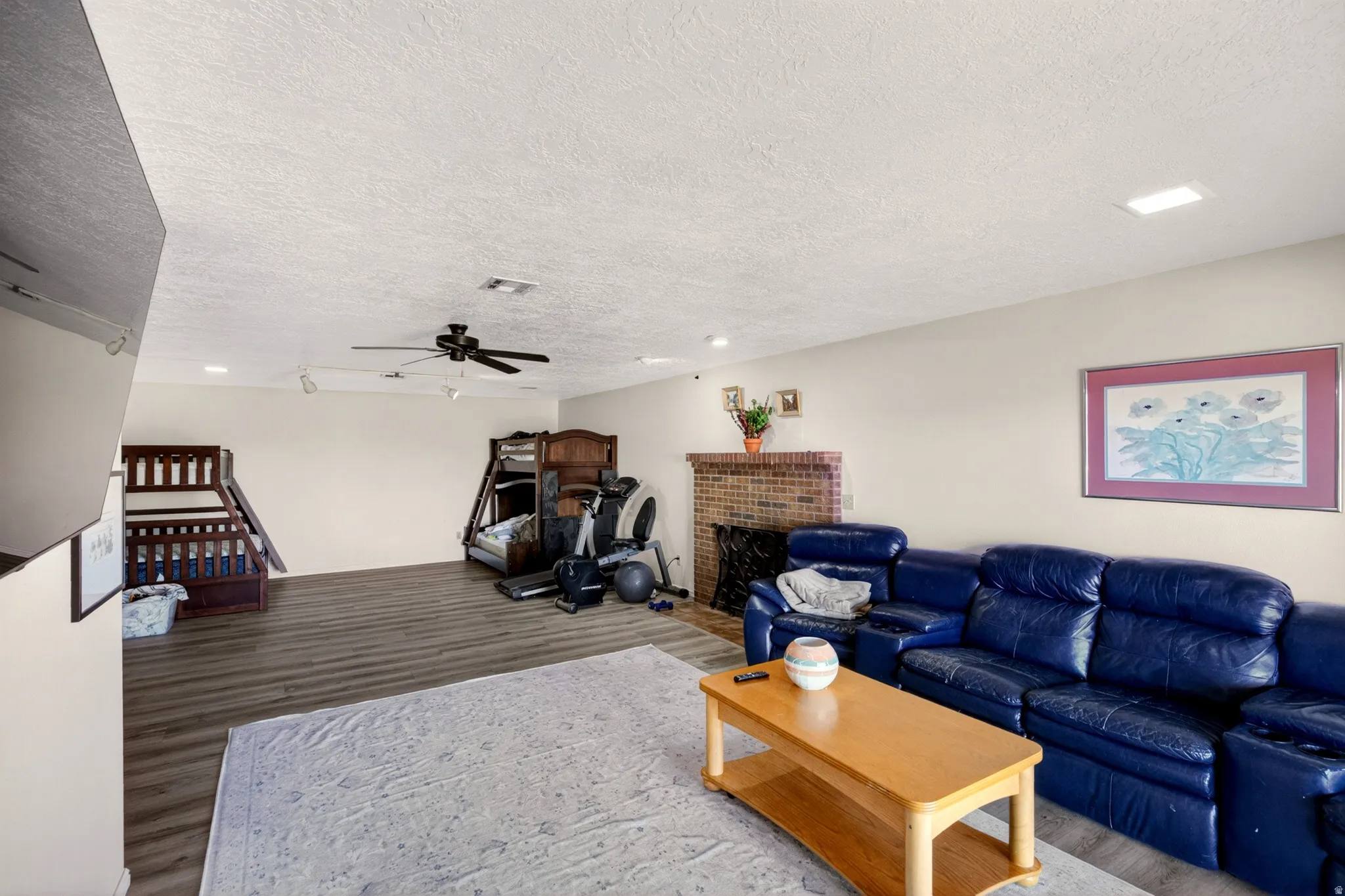 Living area with wood finished floors, a brick fireplace, a textured ceiling, and a ceiling fan