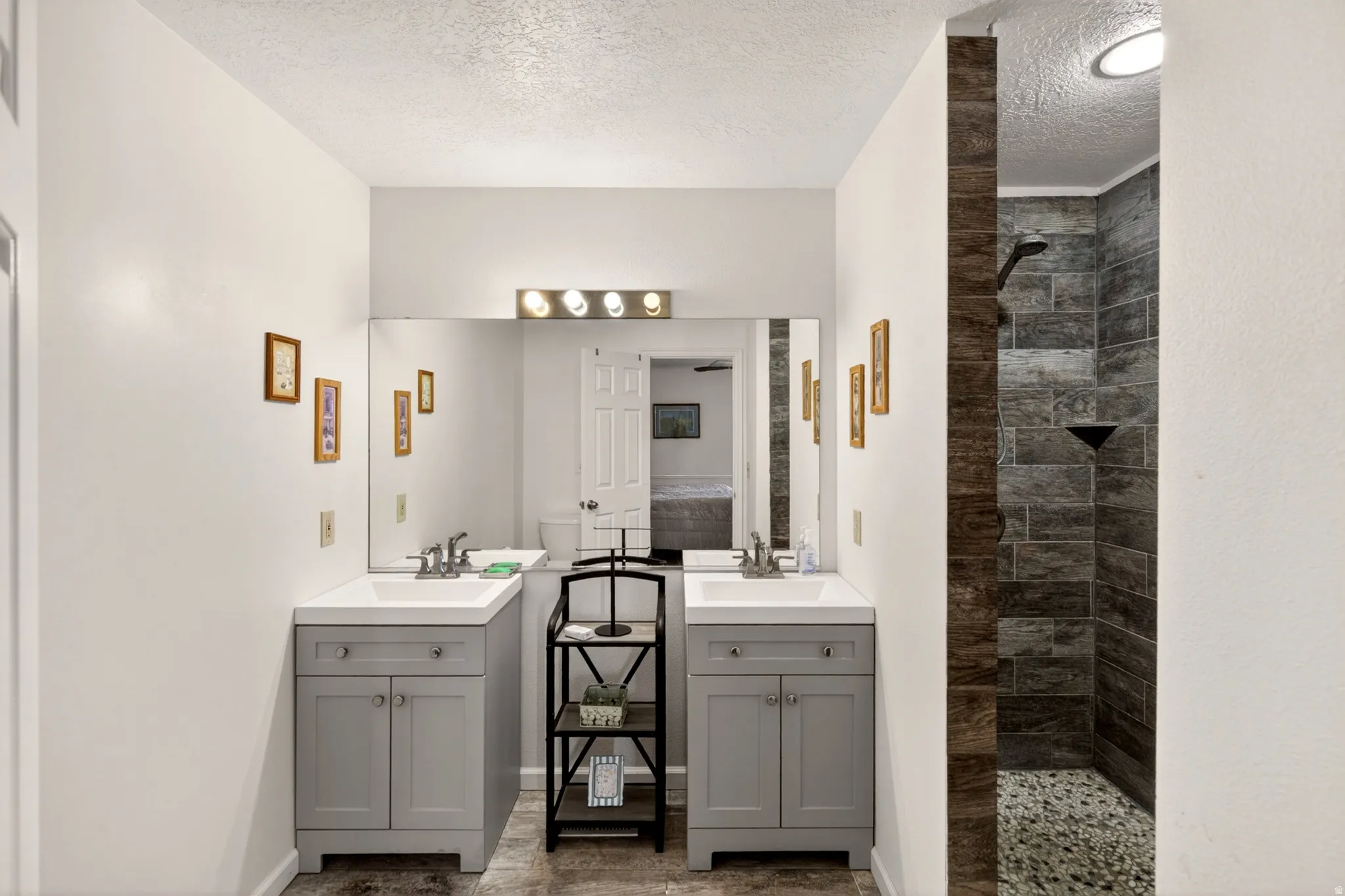 Bathroom featuring a walk in shower, two vanities, and a textured ceiling