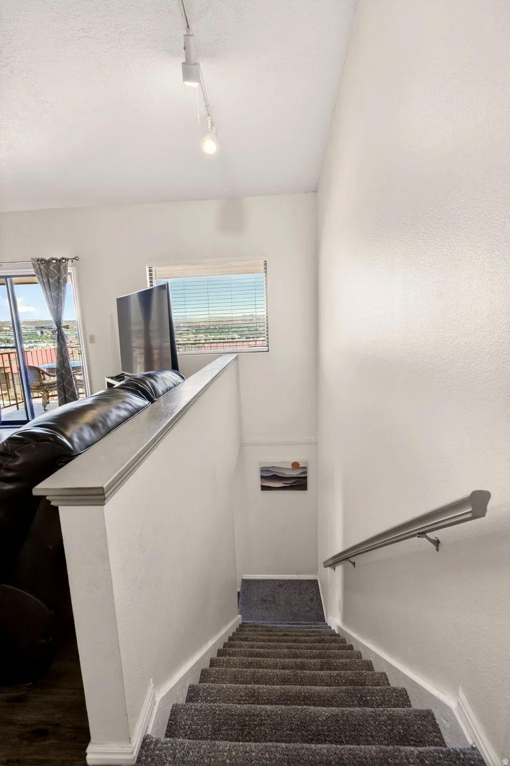 Stairway with plenty of natural light, rail lighting, and a textured ceiling