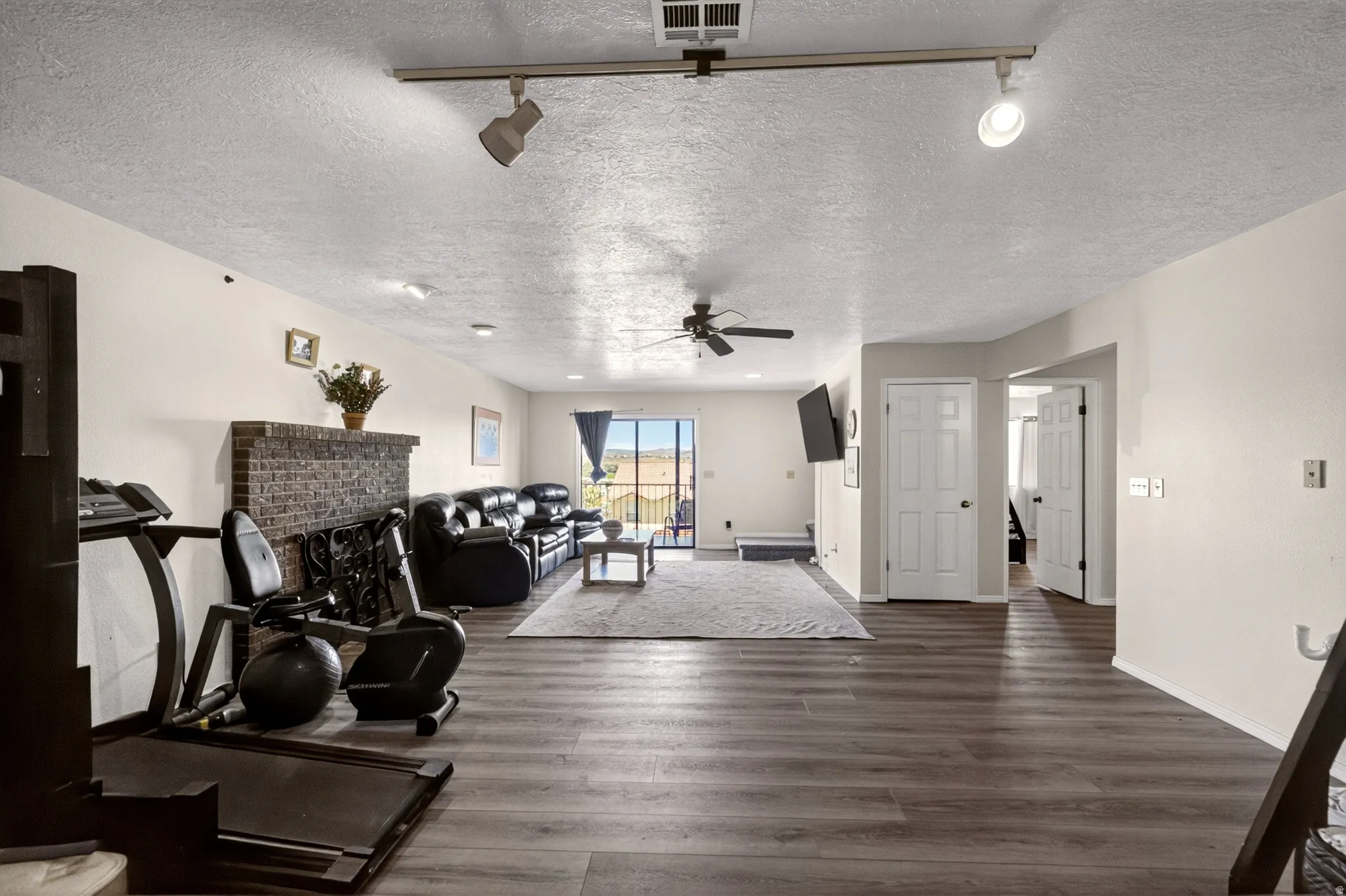 Living area with track lighting, dark wood-style floors, a textured ceiling, ceiling fan, and a brick fireplace