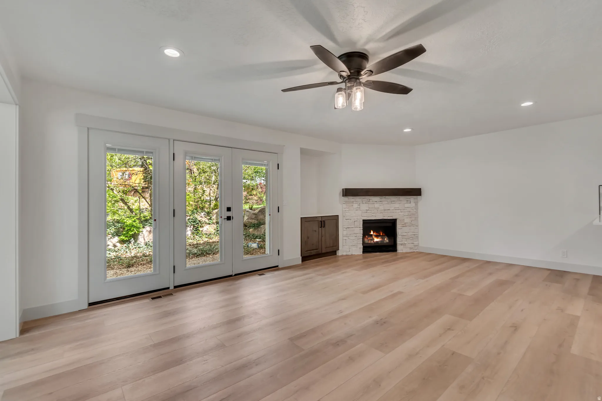 Unfurnished living room featuring light wood-style flooring, ceiling fan, recessed lighting, and a stone fireplace