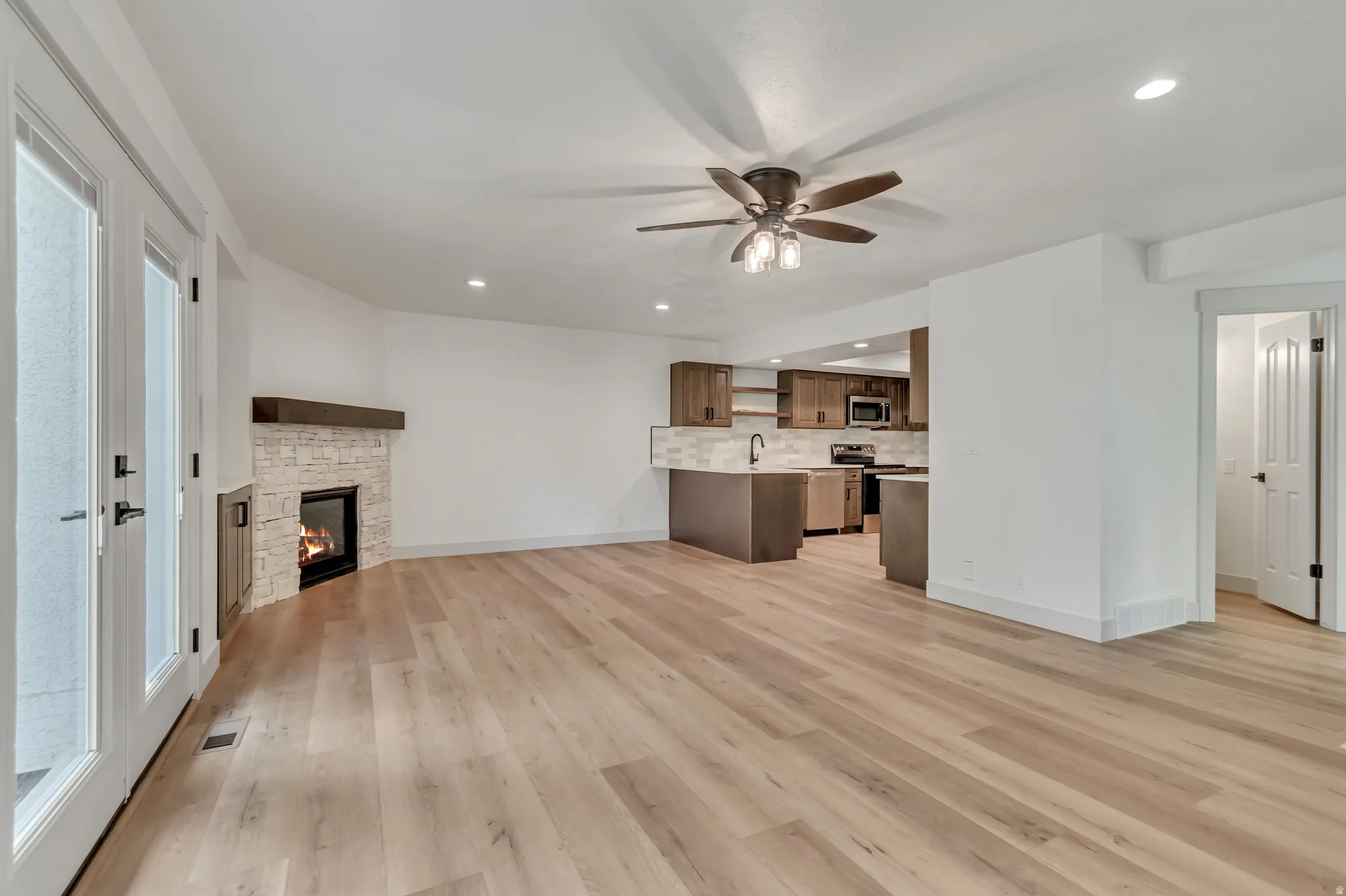Unfurnished living room featuring recessed lighting, ceiling fan, a stone fireplace, and light wood-style flooring