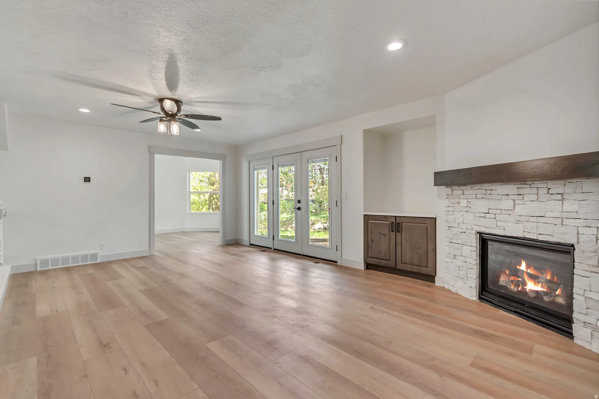 Unfurnished living room featuring ceiling fan, french doors, a stone fireplace, recessed lighting, and light wood finished floors