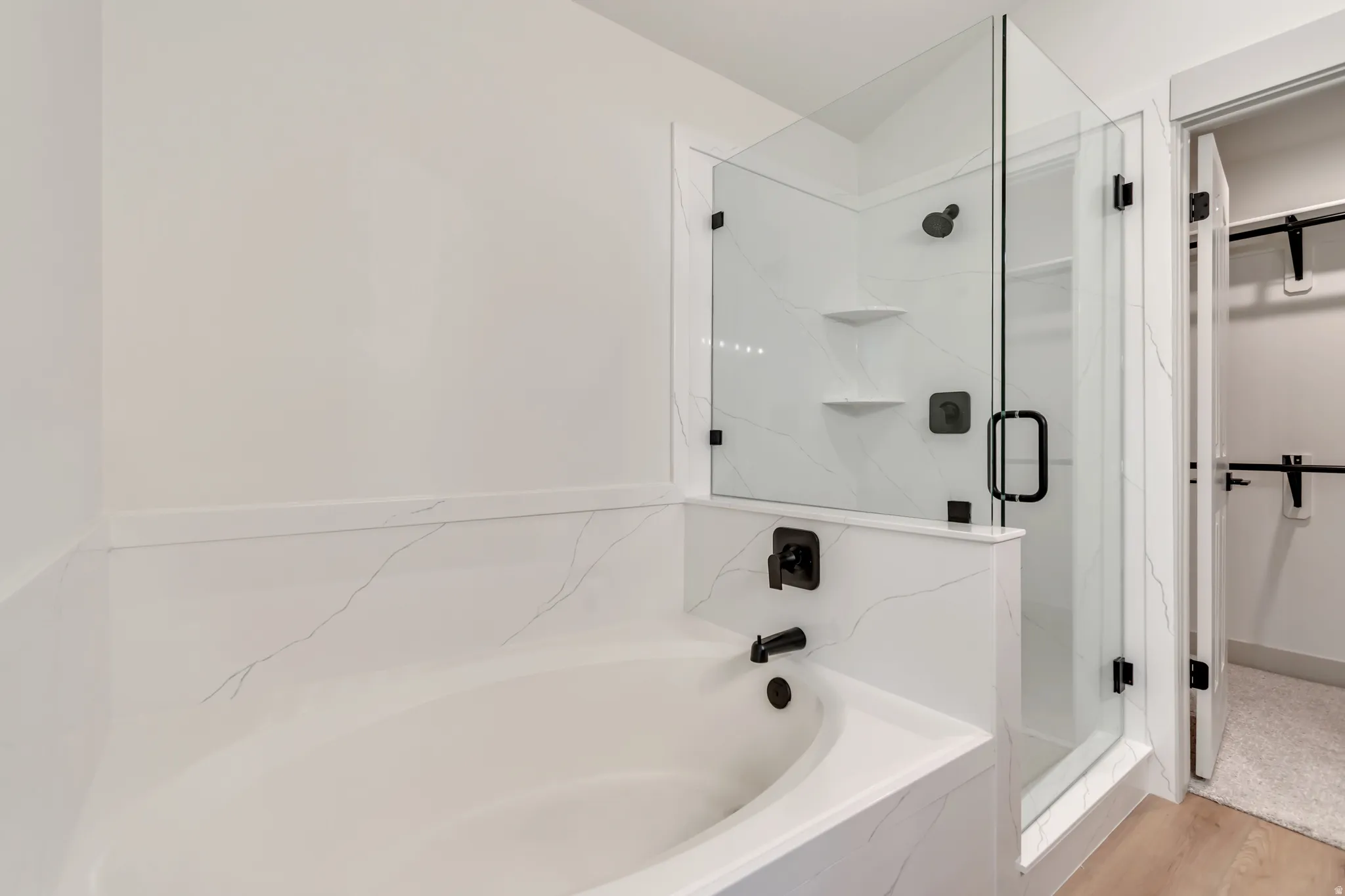 Full bathroom with a walk in closet, a marble finish shower, a garden tub, and light wood finished floors