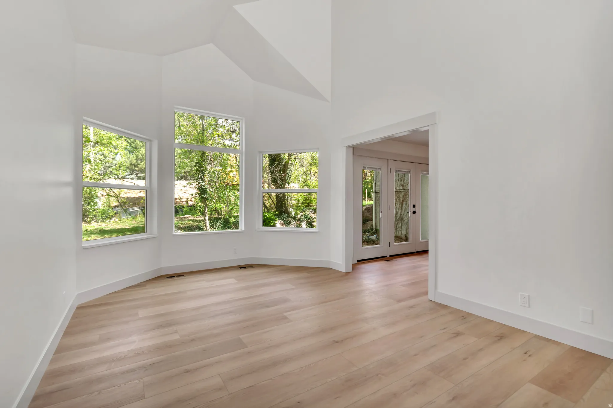 Unfurnished room featuring french doors, light wood finished floors, and lofted ceiling