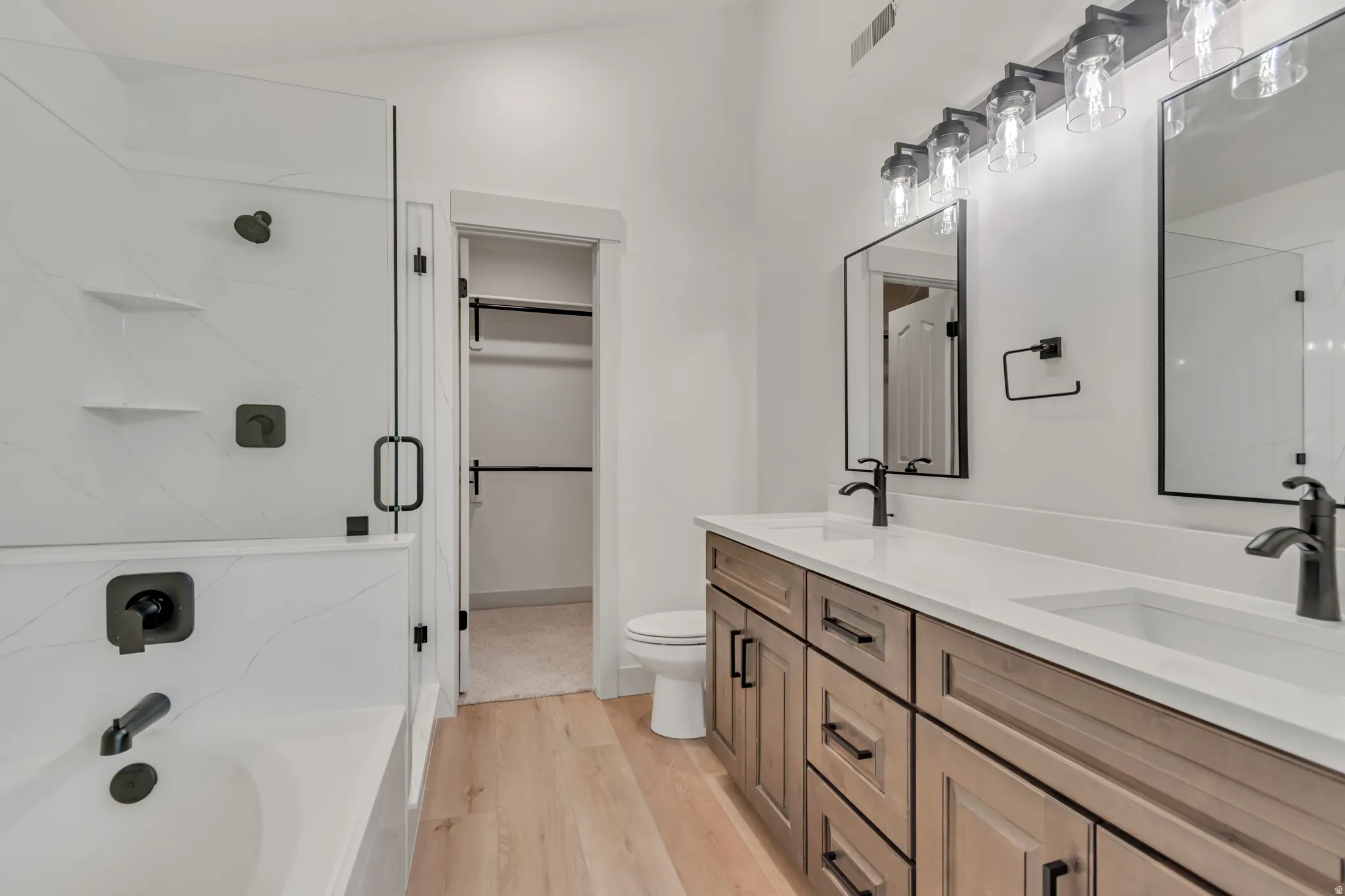 Full bath featuring double vanity, light wood-type flooring, a stall shower, a spacious closet, and a bath