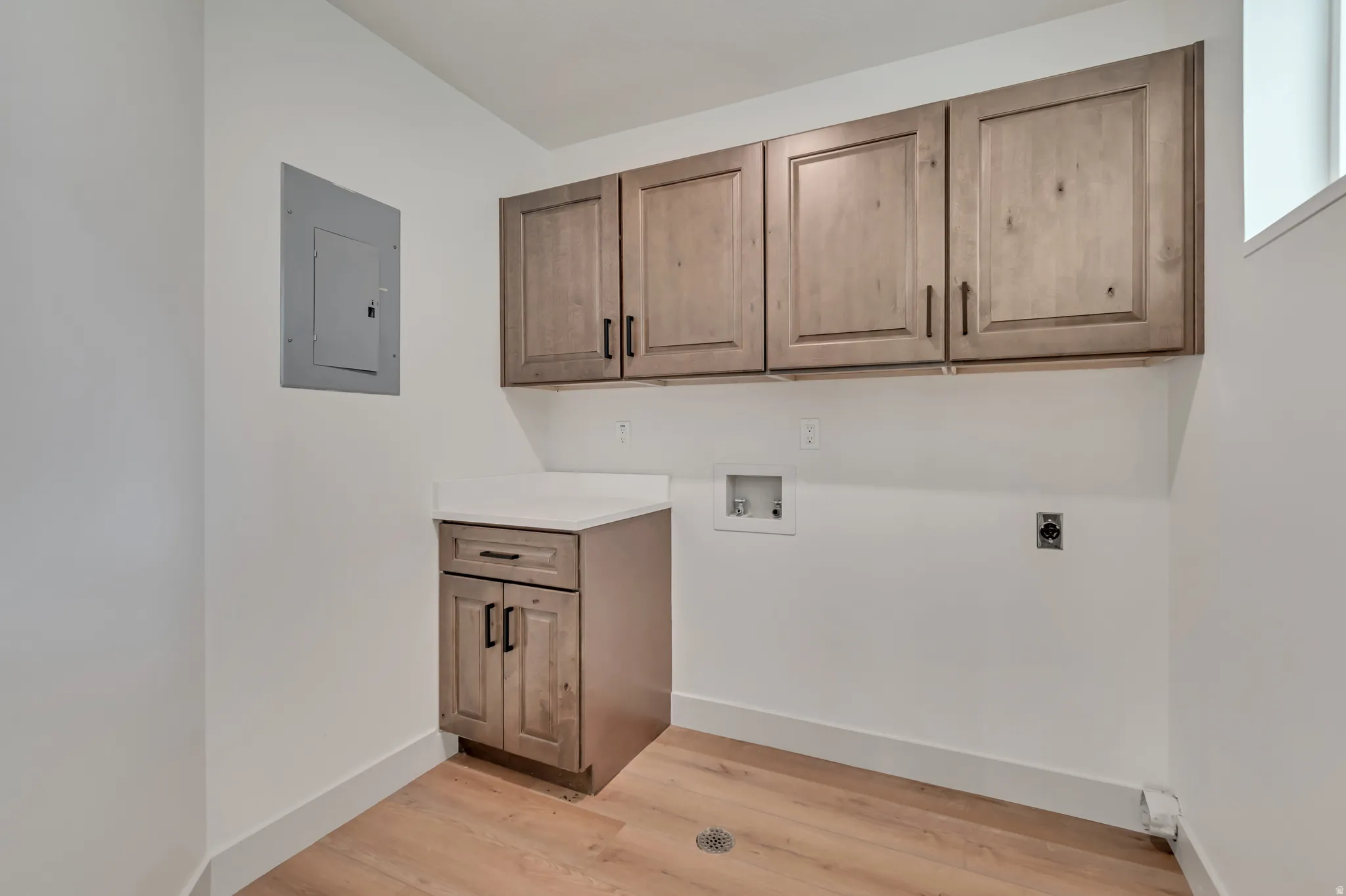 Laundry area with electric panel, hookup for a washing machine, cabinet space, electric dryer hookup, and light wood-type flooring
