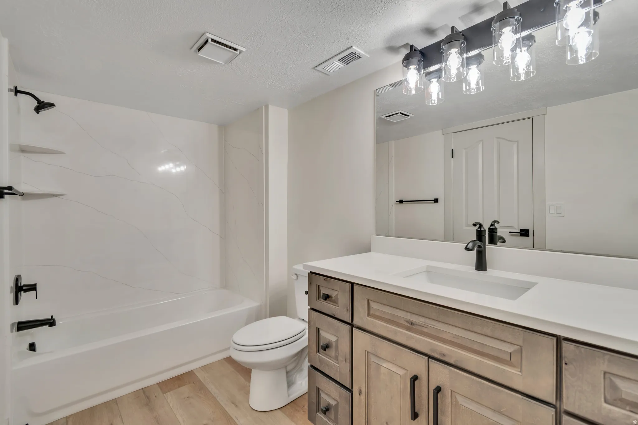 Bathroom with vanity, light wood-style flooring,  shower combination, and a textured ceiling