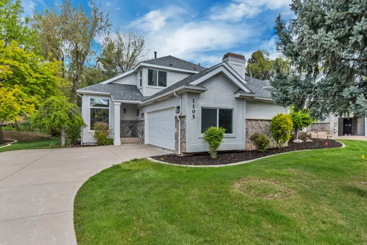 View of front facade with stone siding, stucco siding, concrete driveway, a front yard, and a chimney