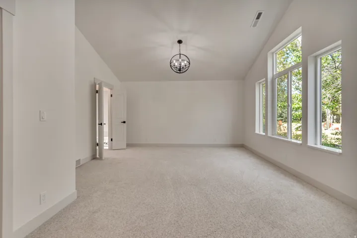 Spare room with vaulted ceiling, a chandelier, and light carpet