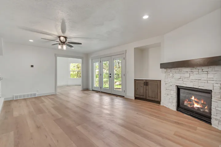 Unfurnished living room featuring ceiling fan, french doors, a stone fireplace, recessed lighting, and light wood finished floors
