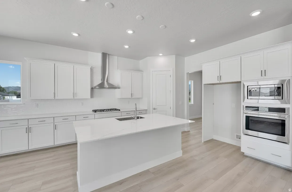 Kitchen with stainless steel appliances, light stone countertops, white cabinets, a center island with sink, and light wood-style floors