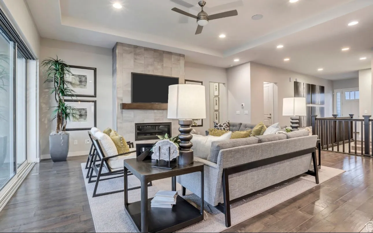 Living room with a ceiling fan, a tray ceiling, dark wood-style flooring, recessed lighting, and a fireplace