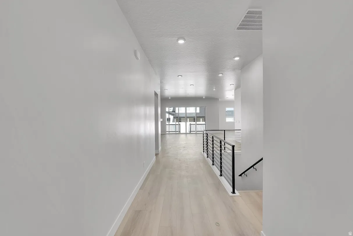 Hall with an upstairs landing, light wood finished floors, recessed lighting, and a textured ceiling