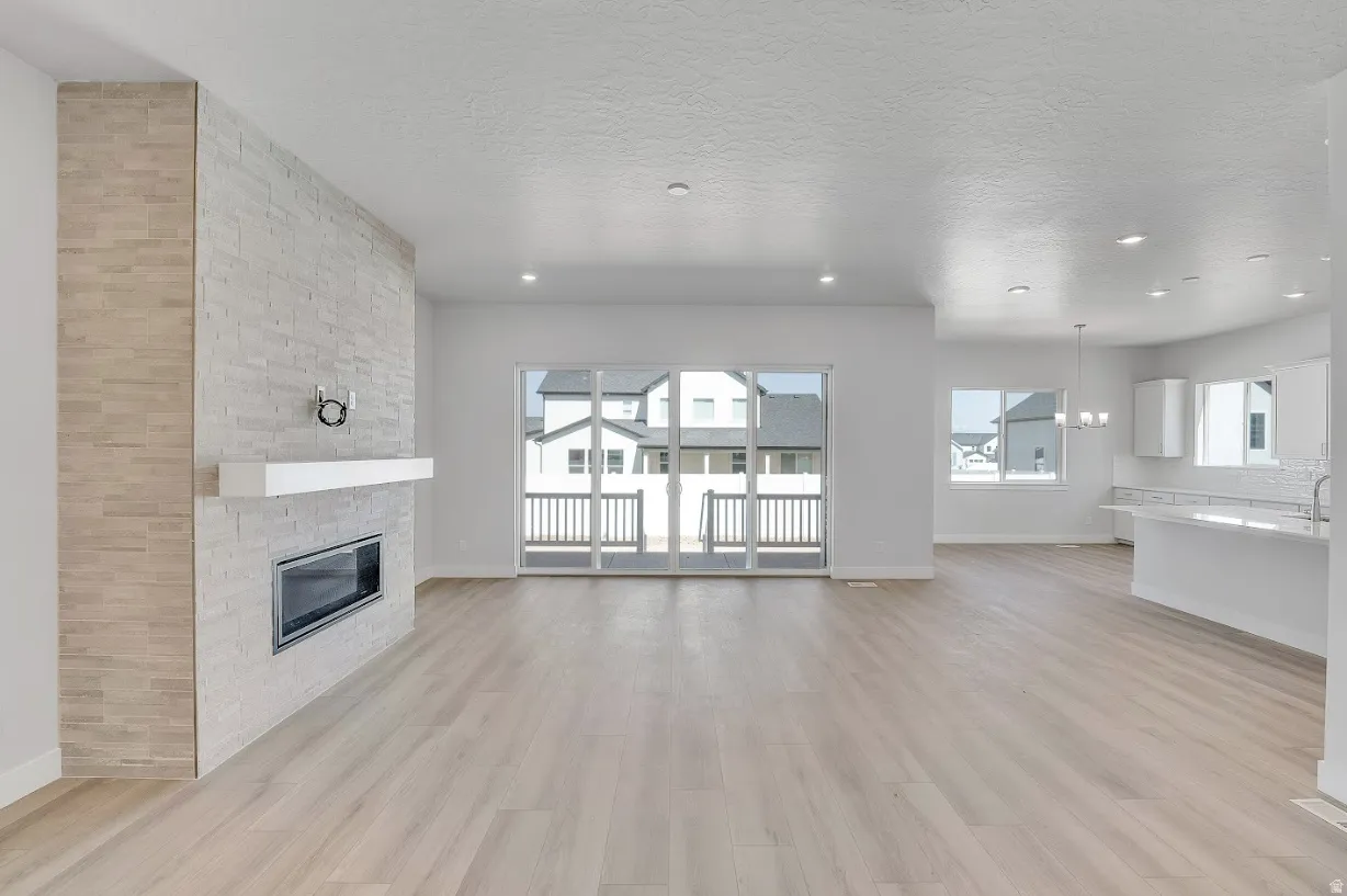 Unfurnished living room featuring light wood-type flooring, a textured ceiling, a fireplace, and hanging lights