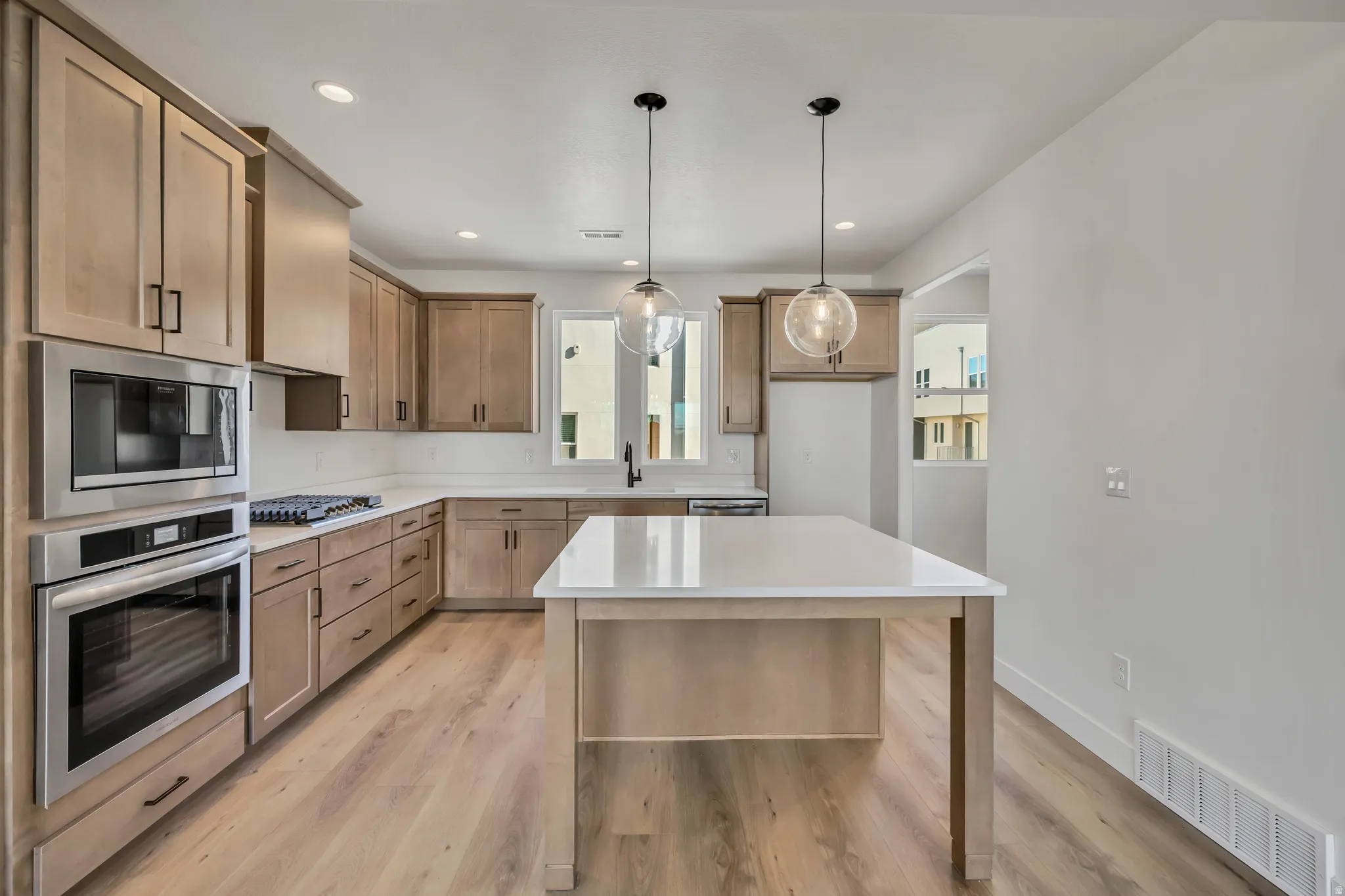 Kitchen with stainless steel appliances, pendant lighting, a kitchen island, light wood finished floors, and wood finish cabinets