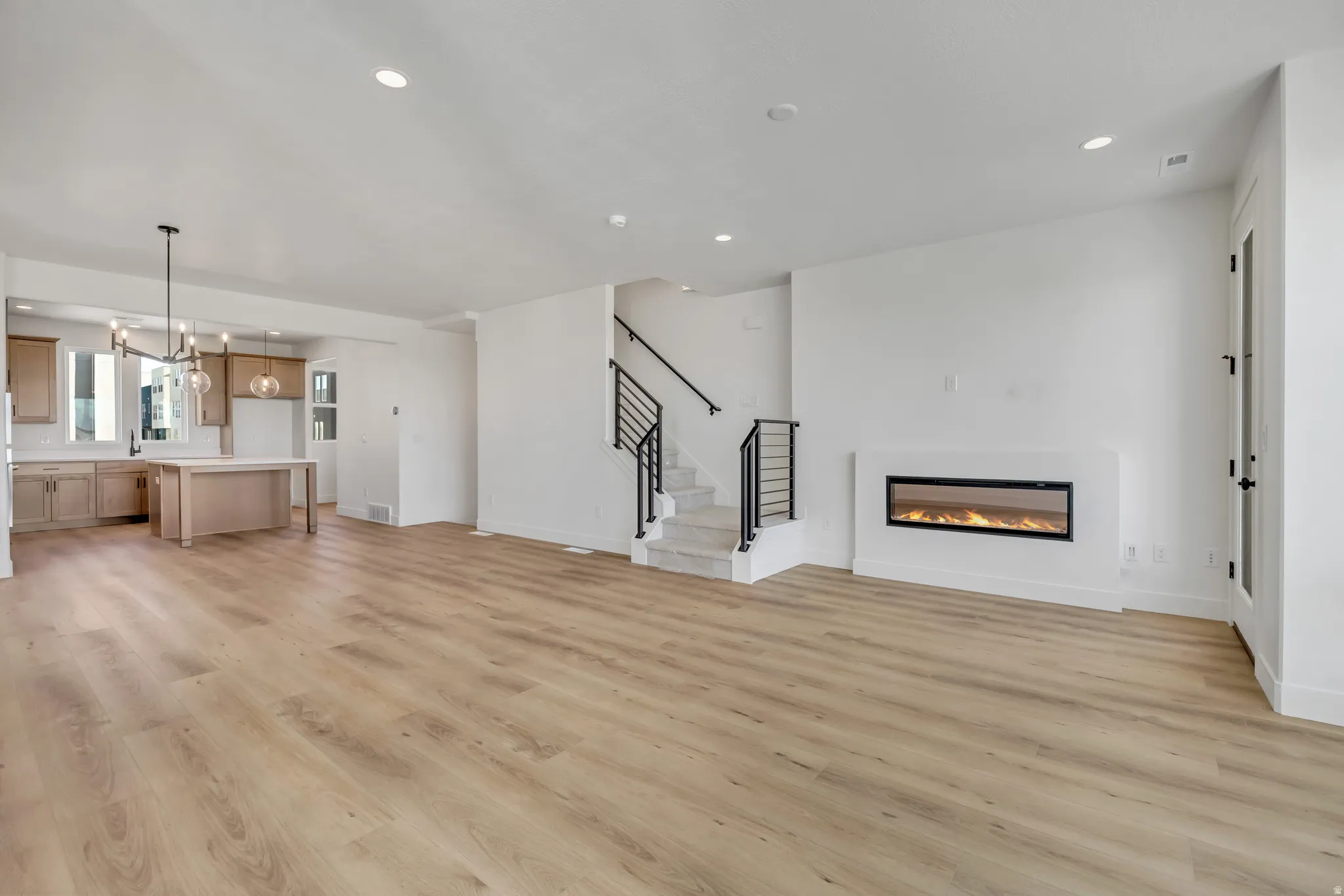 Unfurnished living room with a glass covered fireplace, light wood-style floors, and hanging lights