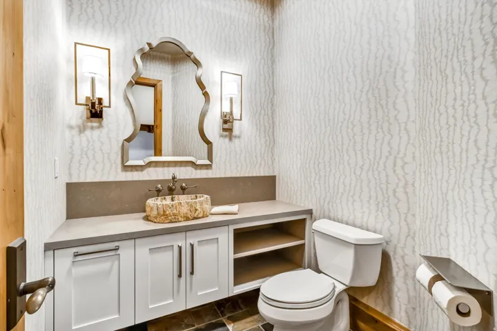 Half bath with wallpapered walls, vanity, and dark stone finish flooring