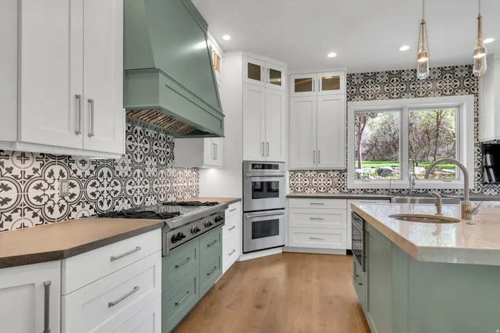 Two tone kitchen with pendant lighting, glass insert cabinets, stainless steel appliances, dark stone counters, and dual tone cabinets