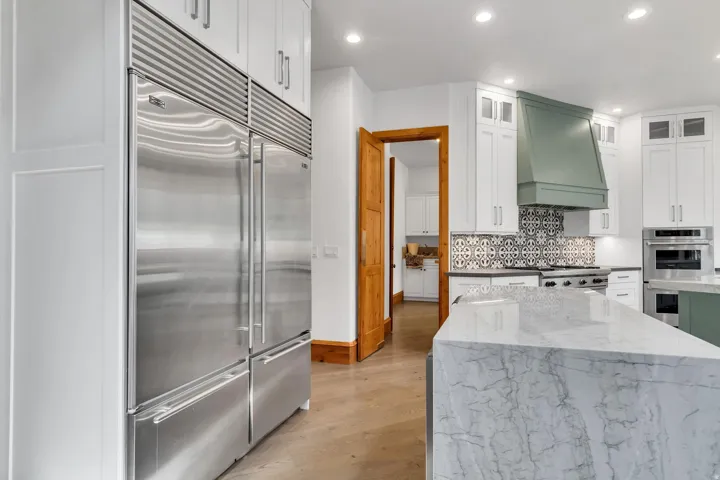 Two tone kitchen with stainless steel appliances, light stone counters, recessed lighting, dual tone cabinetry, and light wood finished floors