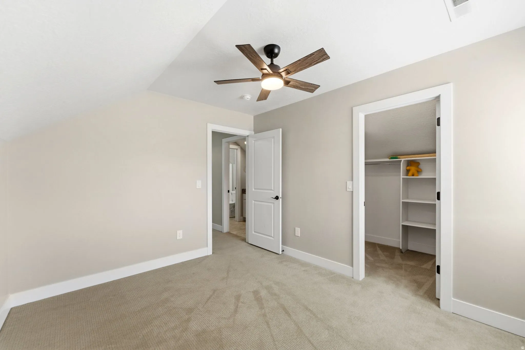 Unfurnished bedroom with a walk in closet, a ceiling fan, light colored carpet, and lofted ceiling